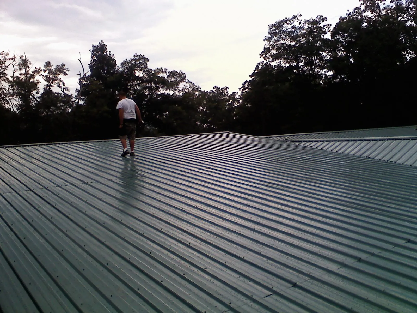 Roofer walking a wide expanse of new green metal roofing in Monroeville